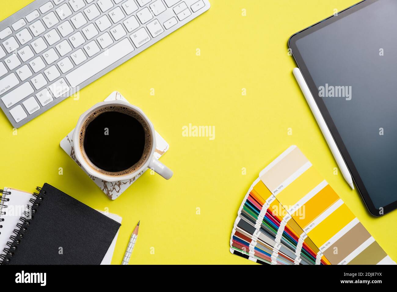 Designer desk top view with computer keyboard, graphic tablet color palette, notebook, cup of coffee on yellow background. Flat lay, view from above. Stock Photo