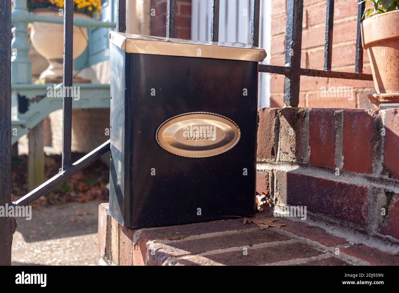 Close up isolated image of a small size vertical mail box that is attached to the railings of the brick outdoor stairs at the entrance of a townhome. Stock Photo