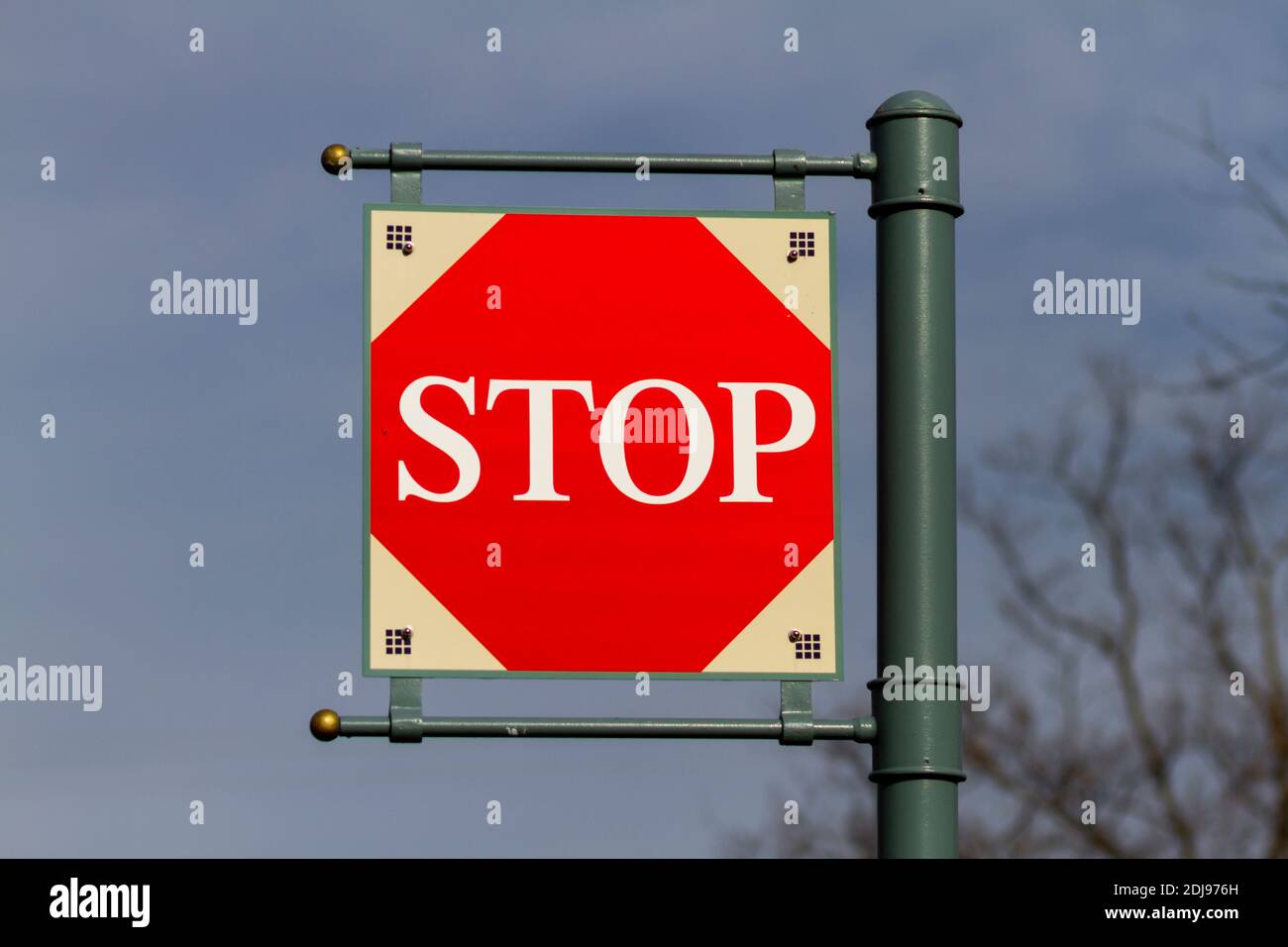 Isolated square shaped STOP sign attached to a metal signpost through hinges and is hanging above against sky. The red part in the sign is octagonal a Stock Photo