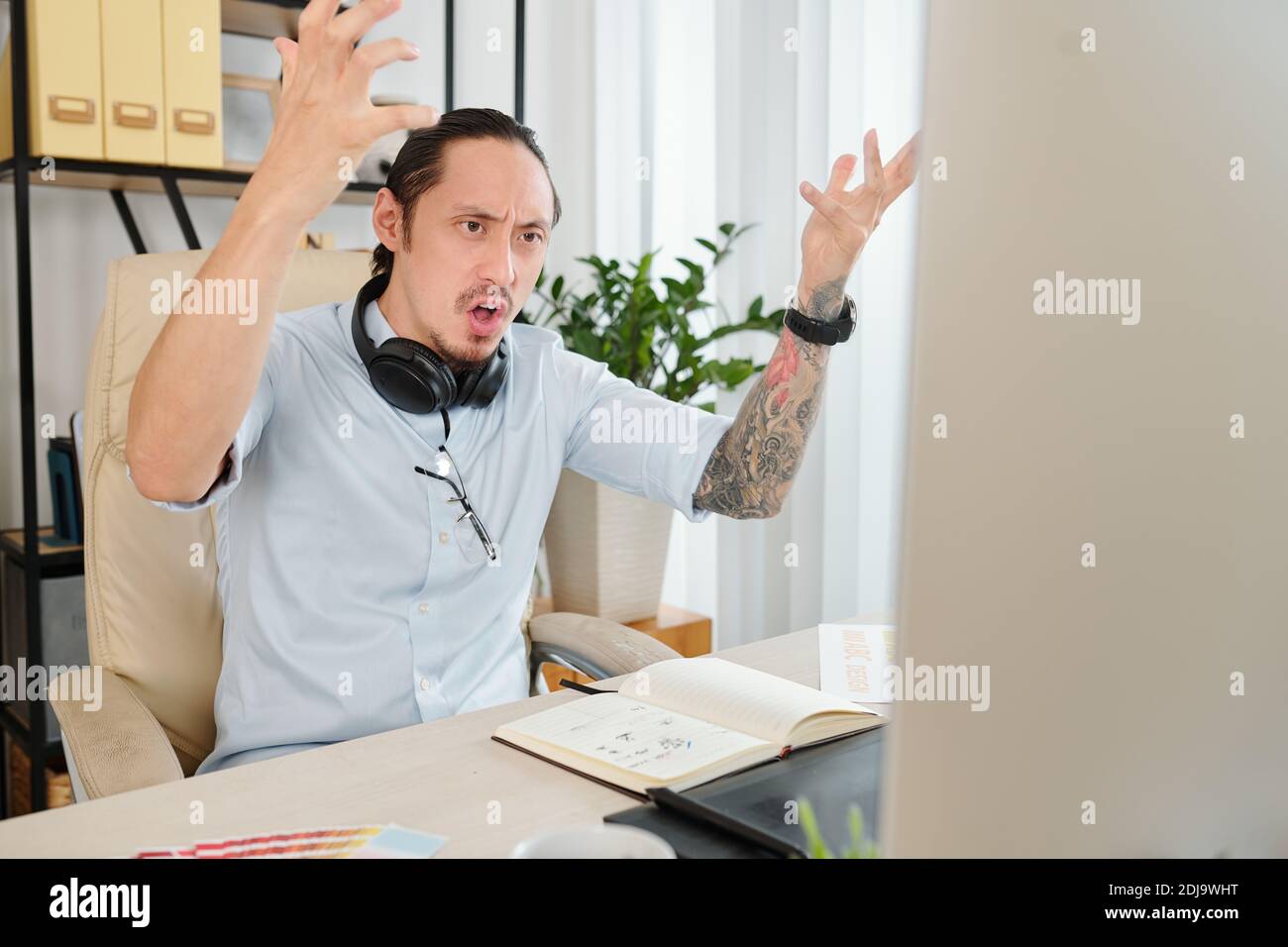 Angry indignant graphic designer actively gesturing after reading e-mail from client asking for a few changes Stock Photo