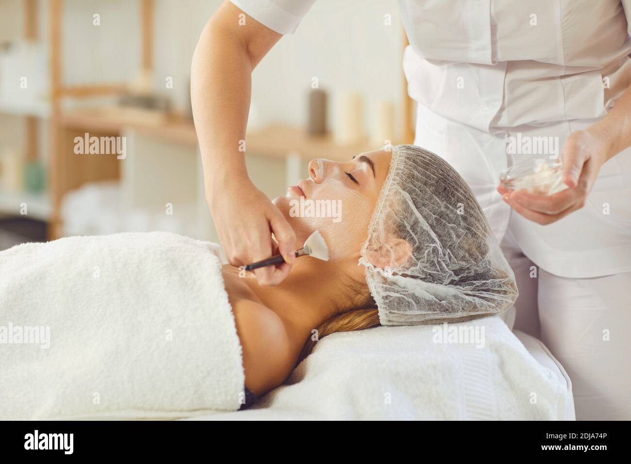 Beautician covering young womans face with moisturizing mask or cream after skincare procedure Stock Photo