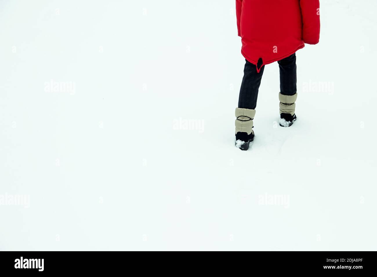 a child walking away in the snow in a red jacket rear view. Stock Photo