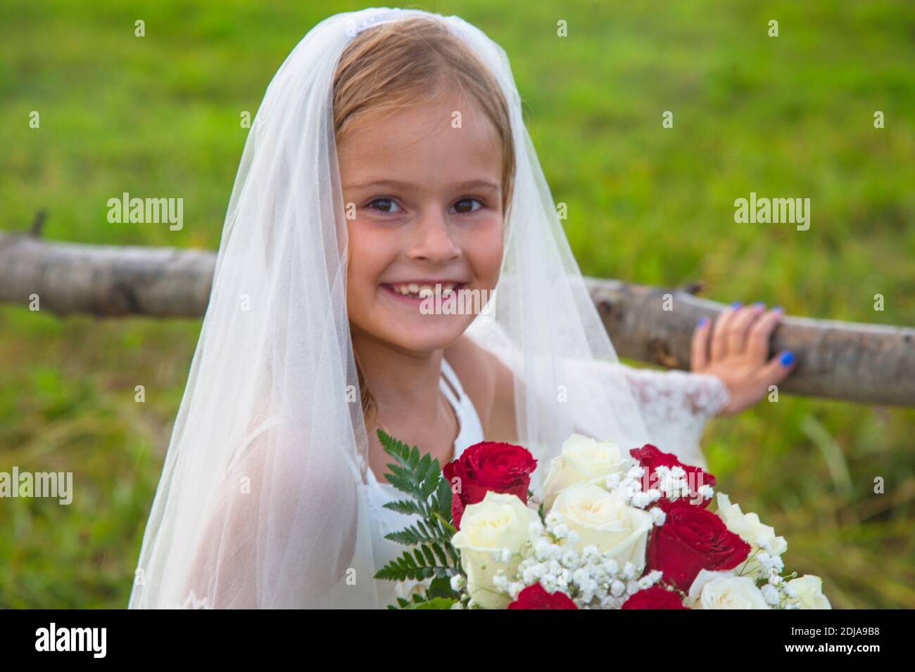 ove is present. Children's day. little girl in a bride's dress with a veil and a wedding bouquet. Beauty. a little girl with a bouquet of red and whit Stock Photo