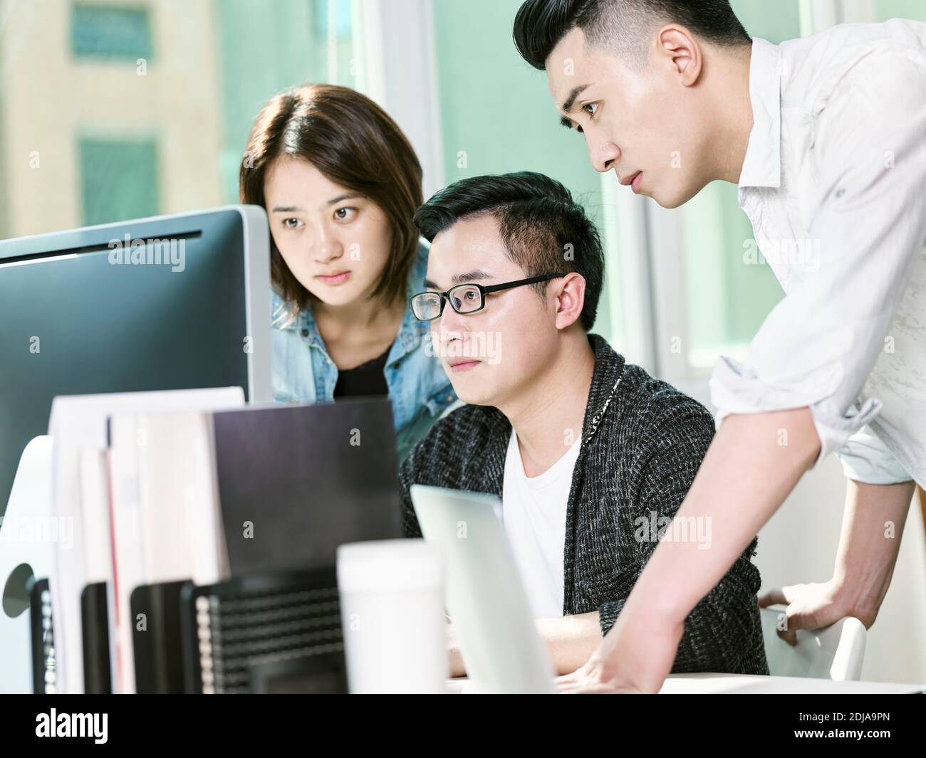 team of three young entrepreneurs analyzing data in office using desktop computer Stock Photo