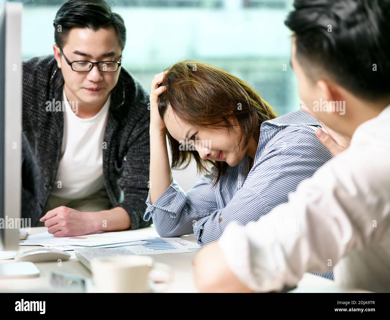 frustrated asian businesswoman getting comfort from colleagues while discussing business in office Stock Photo