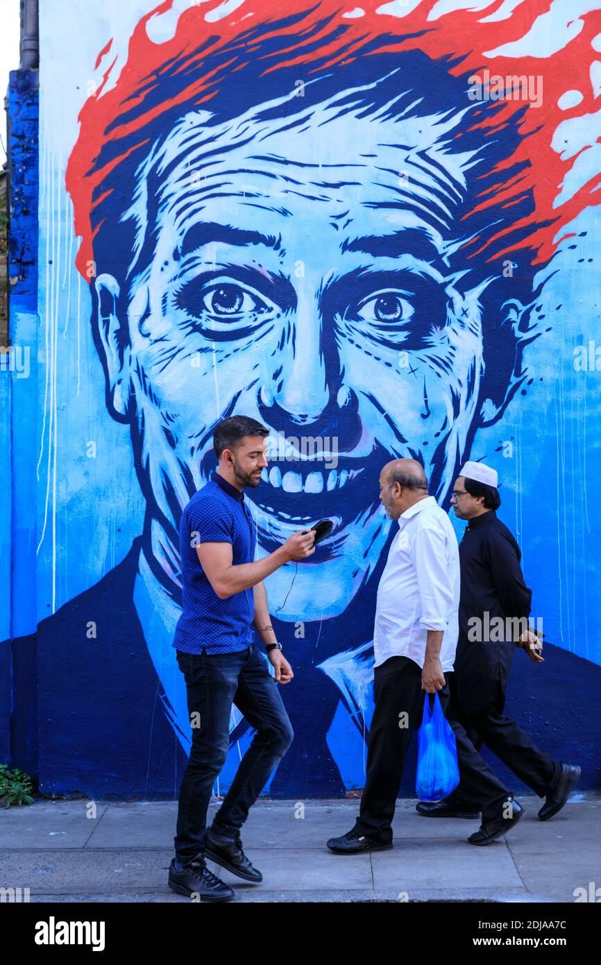 People walking past a street art of a head on fire by Sr.X near Brick Lane, East London, UK Stock Photo