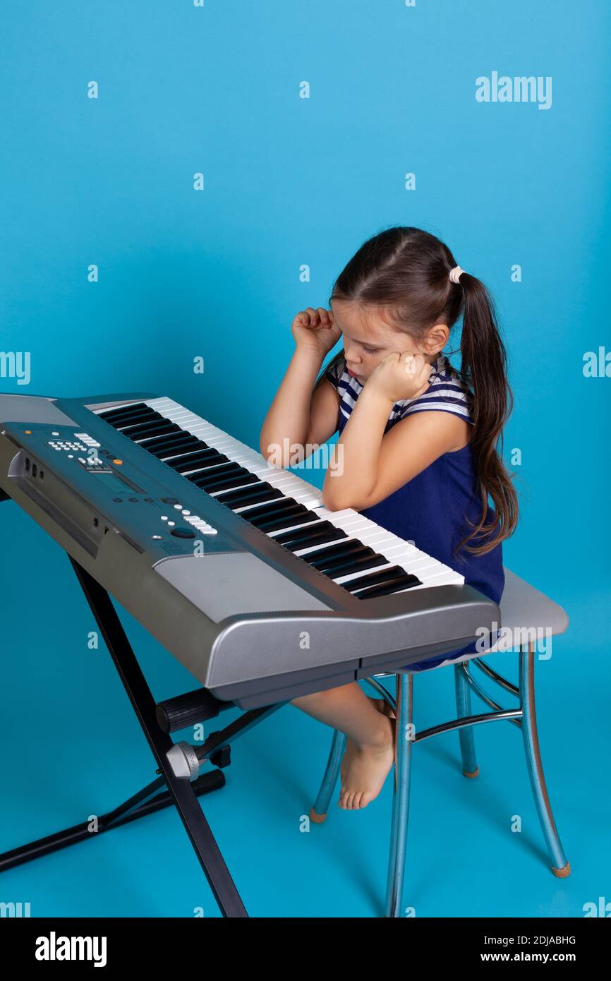 a full-length girl plays music with her elbows on an electronic synthesizer, people with disabilities isolated on a blue background Stock Photo