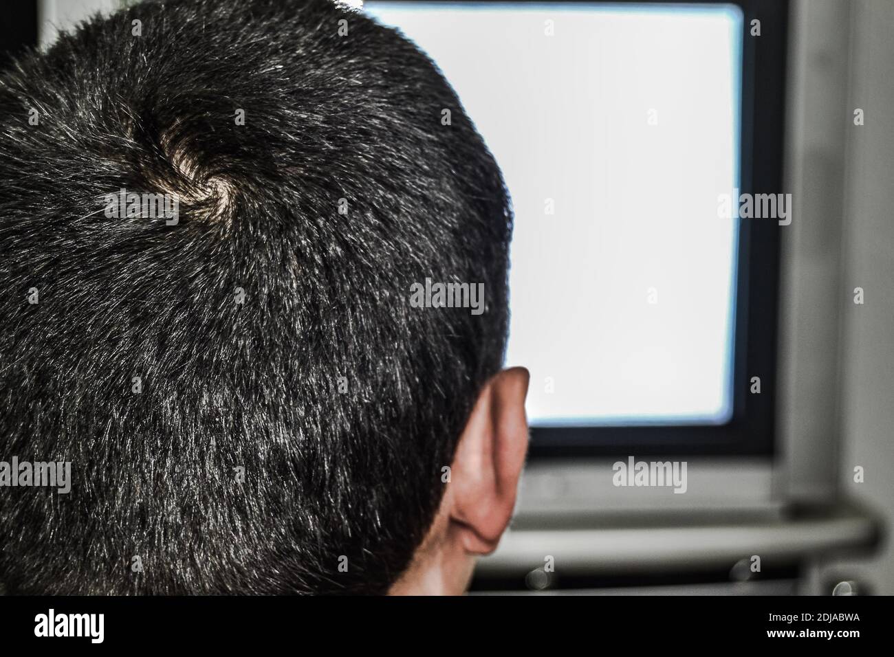 A alone man is watching television. Photo shows behind of the man and his head and also in old style and tube television TV there is grainy screen. Stock Photo