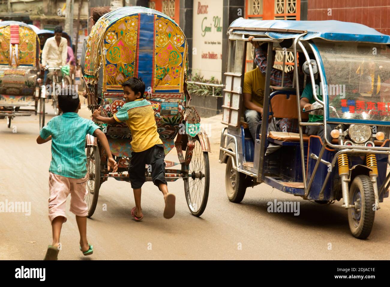 Dhaka, Bangladesh - October 28, 2018: Two kids playing and trying to get on board of a rickshaw, the most common urban mean of transportation. Stock Photo