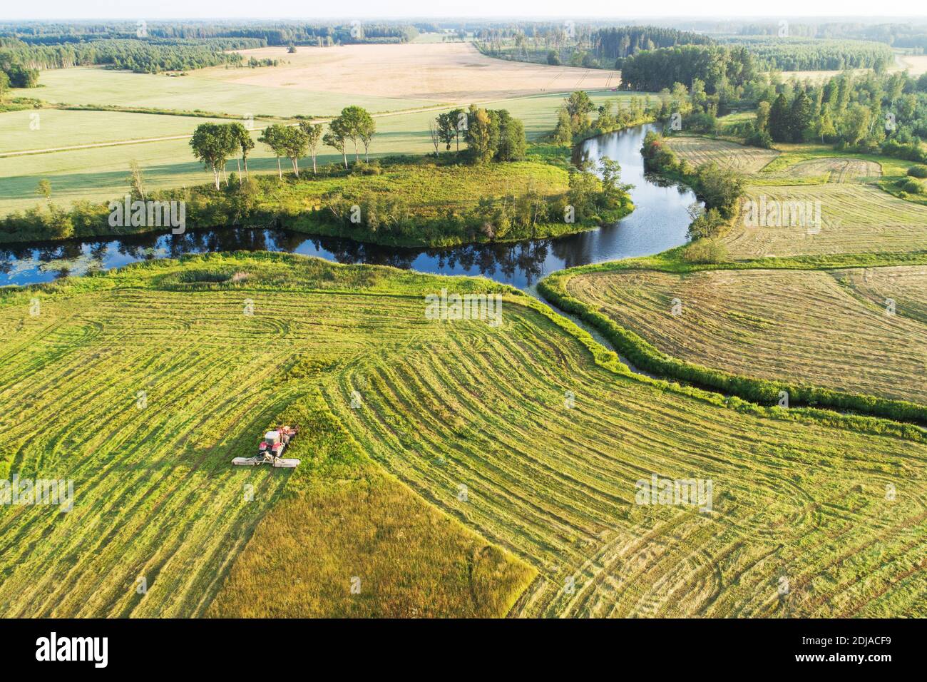 An aerial of a tractor cutting grass on a meadow next to a river during