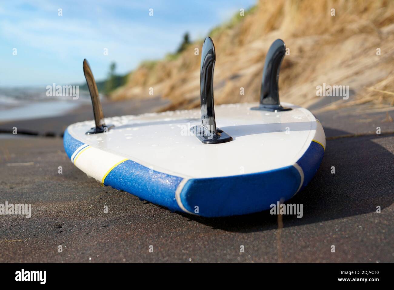 Wet blue and white sup-board closeup lying on the sandy beach with black fins up.  Surf in the background. USA, Michigan, Holland Stock Photo