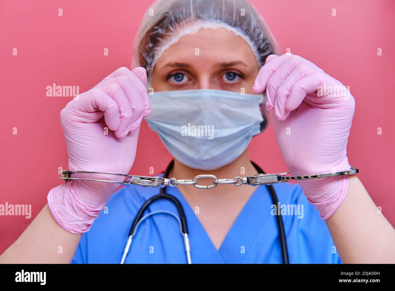 Doctor hands in handcuffs on pink background, close up. Young woman hands in medical gloves handcuffed, coronavirus quarantine concept. Stock Photo