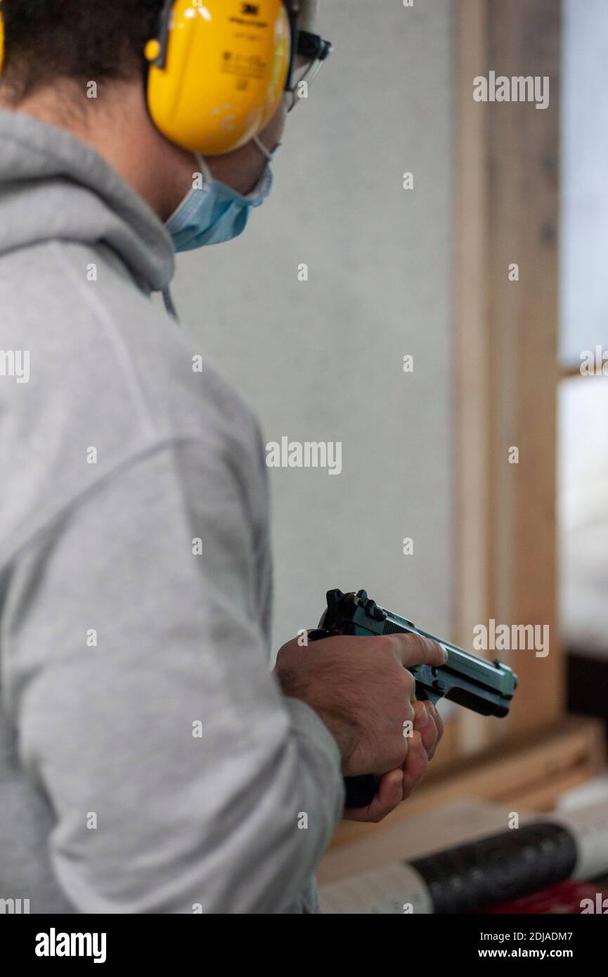 Man at the firing range, with noise reduction headset, automatic pistol in his hand, ready to shoot. Stock Photo