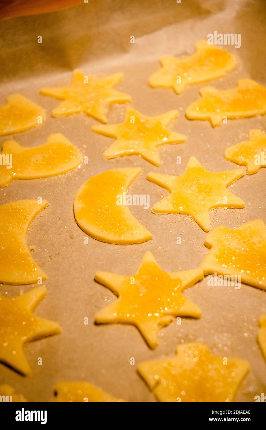 Homemade golden cookies in shapes for christmas, x-mas holidays, on brown baking paper on a tray, preparing, before baking, sweet sugar dessert Stock Photo