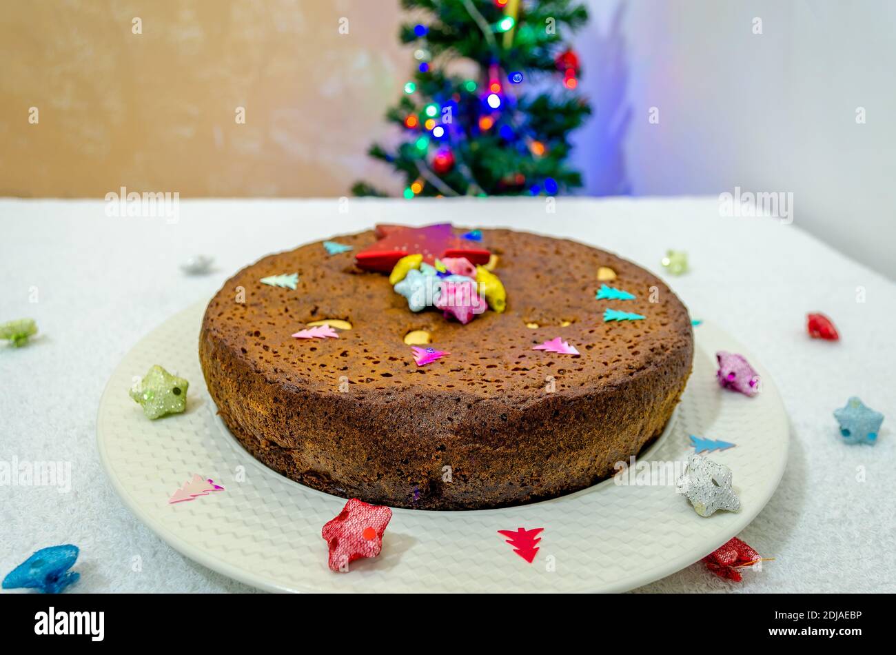 Christmas Special plum cake in a white plate with Christmas decorations and a Christmas tree in the background Stock Photo