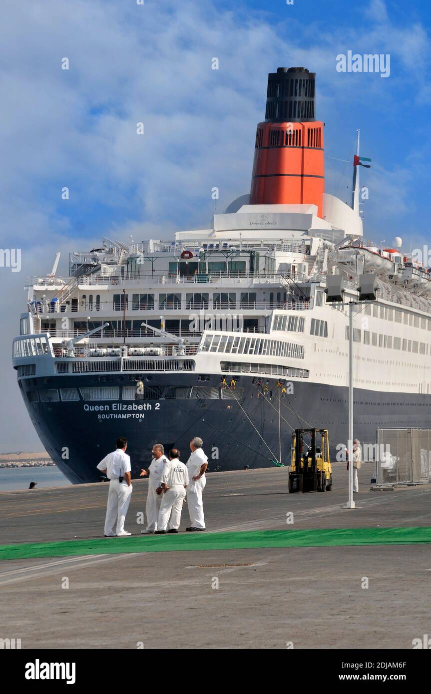 Group of officers & crew from out of shot Costa cruise ship Port Rashid backdrop of Queen Elizabeth 2 QE2 QEII ex Cunard liner awaiting refit as hotel Stock Photo