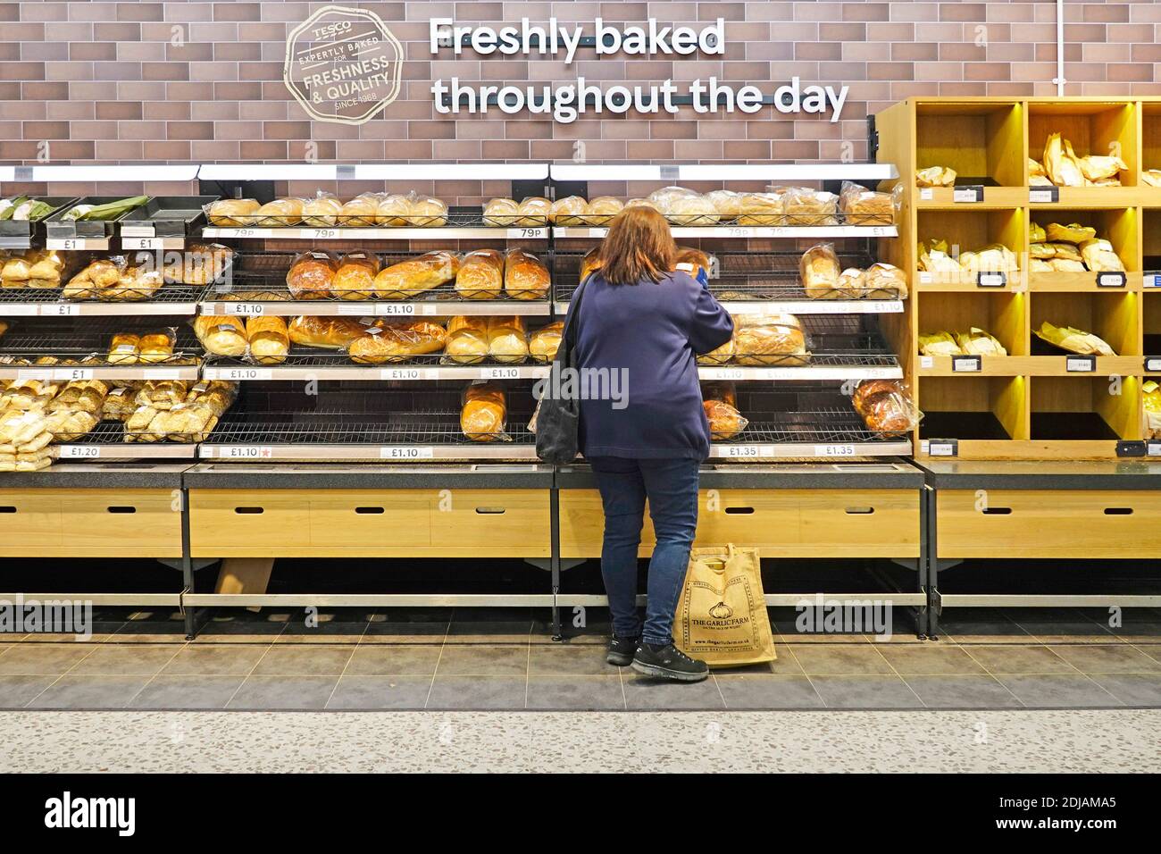 Back view of customer shopping for bread at Tesco supermarket in store bakery selection shelves below sign for freshly baked all day London England UK Stock Photo