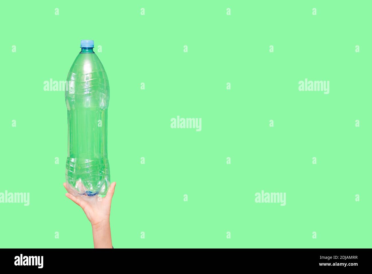 Kid hand holding plastic bottle without water isolated on green background. Ecology environment problem consumption. Reducing consumption of plastics Stock Photo