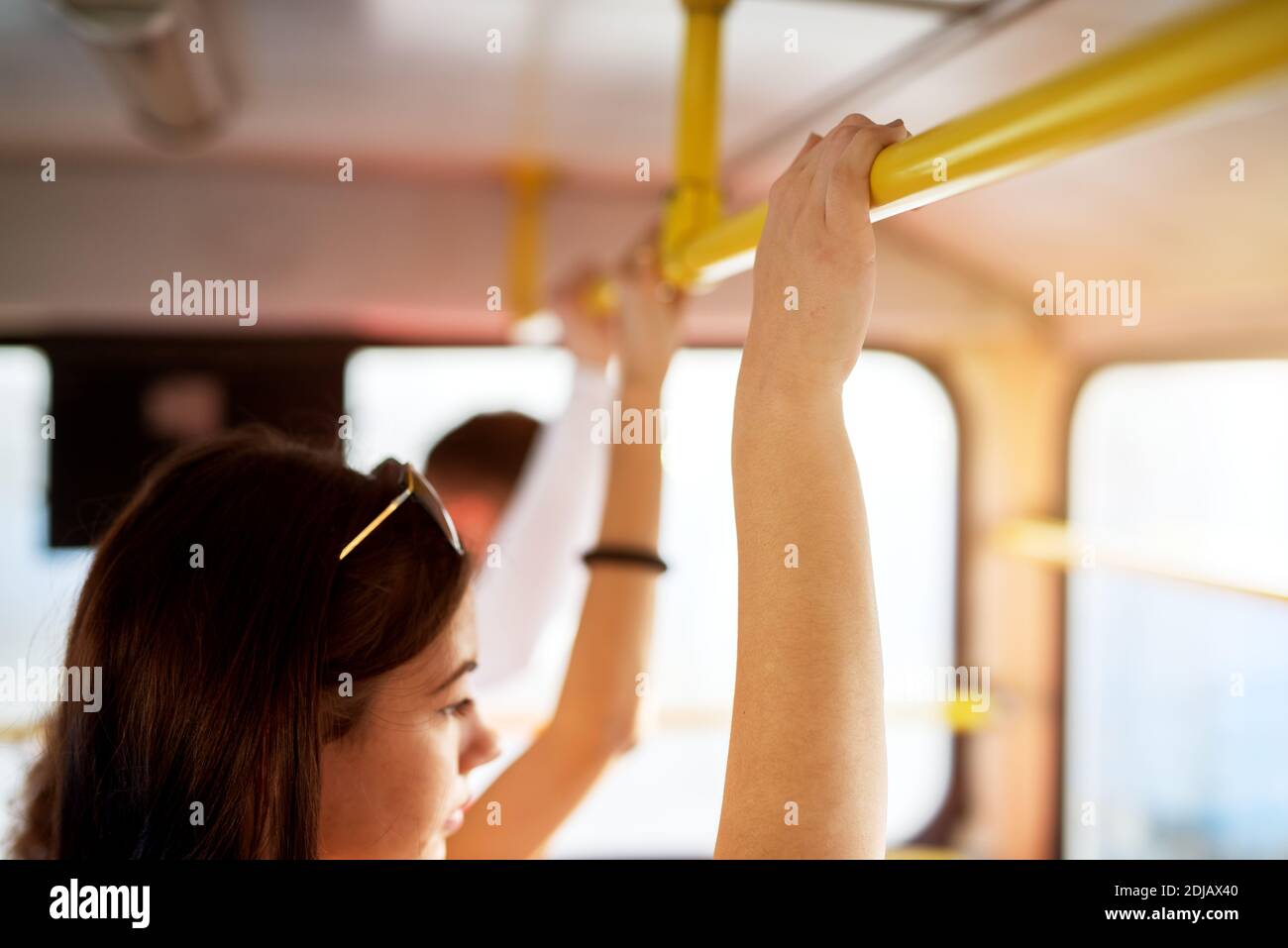A young woman is traveling with bus while standing and holding onto bars. Stock Photo