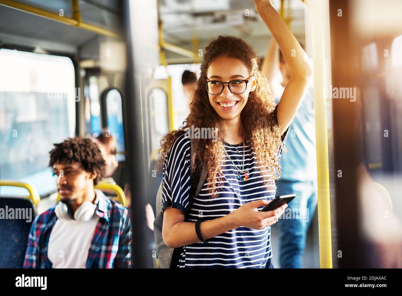 Young gorgeous cheerful woman is standing on the bus using the phone and smiling. Stock Photo