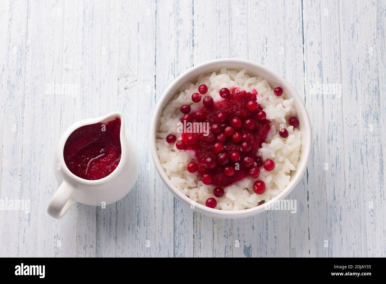Rice pudding with cranberry jam and fresh cranberries in a white bowl on a light blue background, selective focus. Delicious traditional breakfast Stock Photo