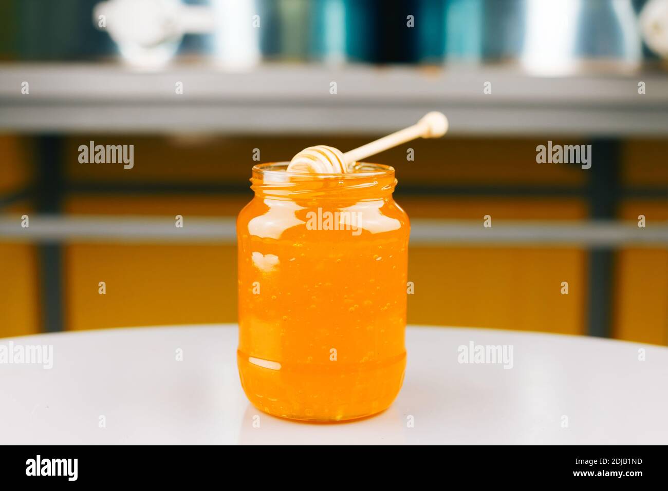 A jar full of honey with a wooden dipper on is standing on a table Stock Photo