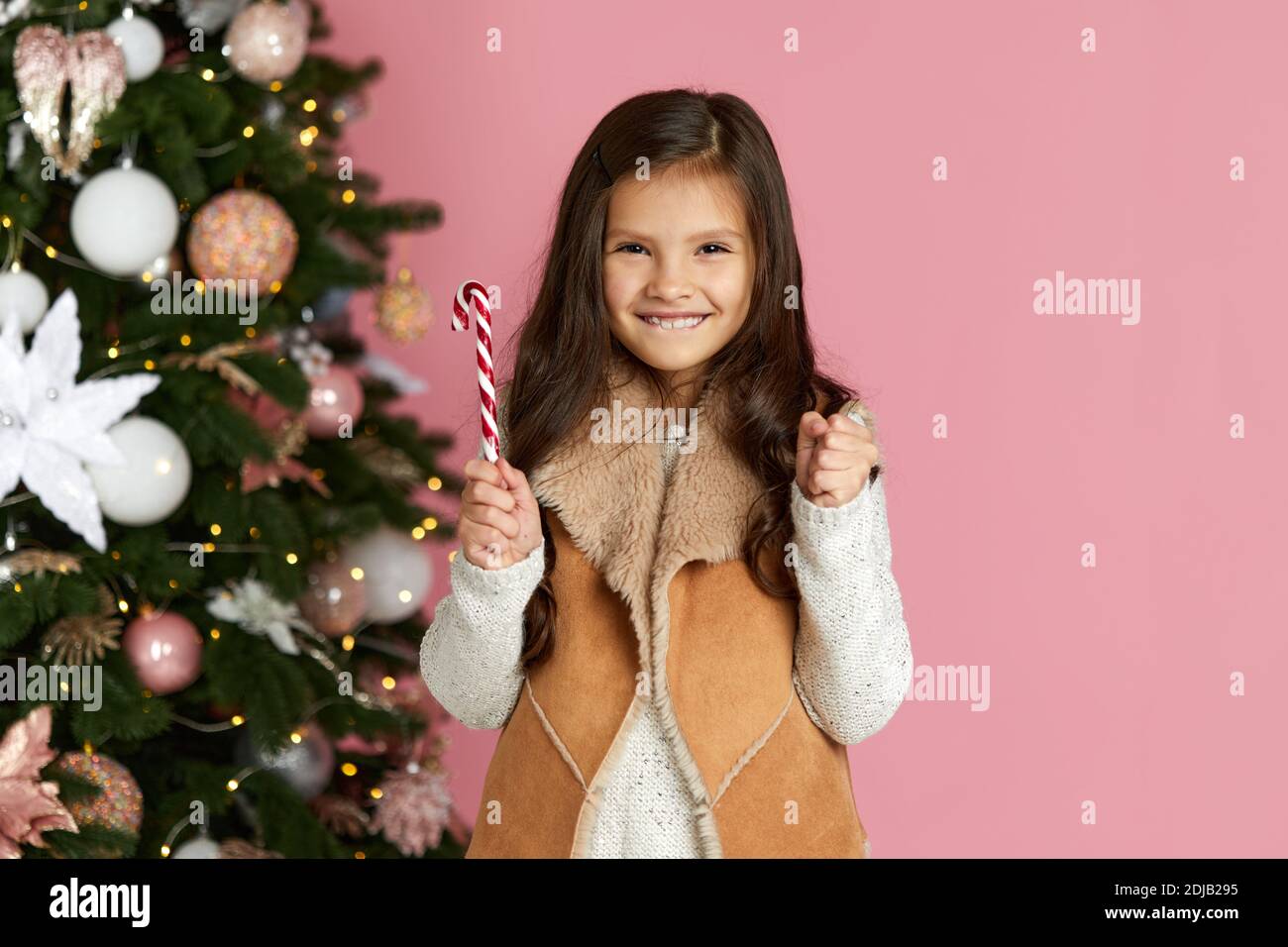 happy little child girl holding lollipop candy cane on the pink background of christmas tree. copy space Stock Photo