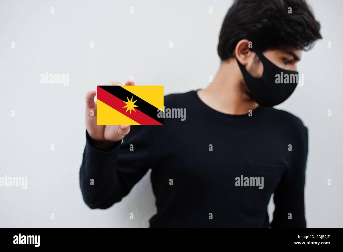 Malay man wear all black with face mask hold Sarawak flag in hand isolated on white background. States and federal territories of Malaysia coronavirus Stock Photo