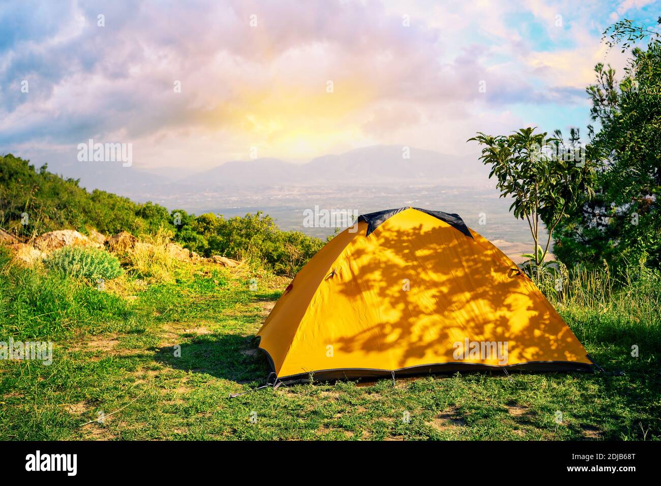 Orange tent on hill with mountains in background at sunrise Stock Photo