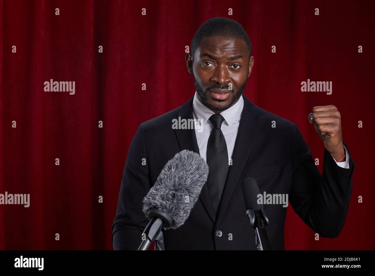 Waist up portrait of African-American man giving speech standing at podium on stage against red curtain, copy space Stock Photo