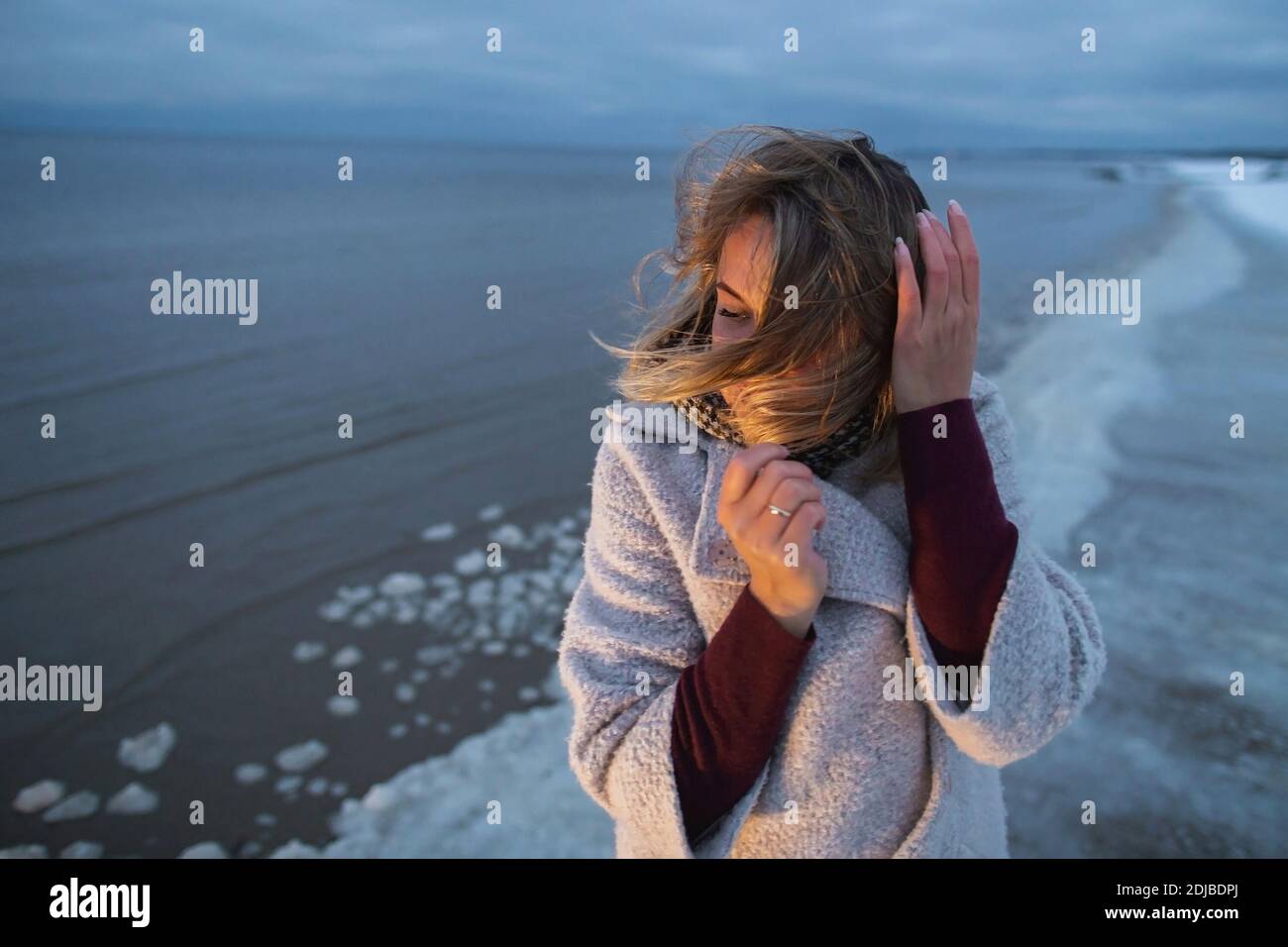Beautiful woman on the winter sea coast evening time warm light. Stock Photo