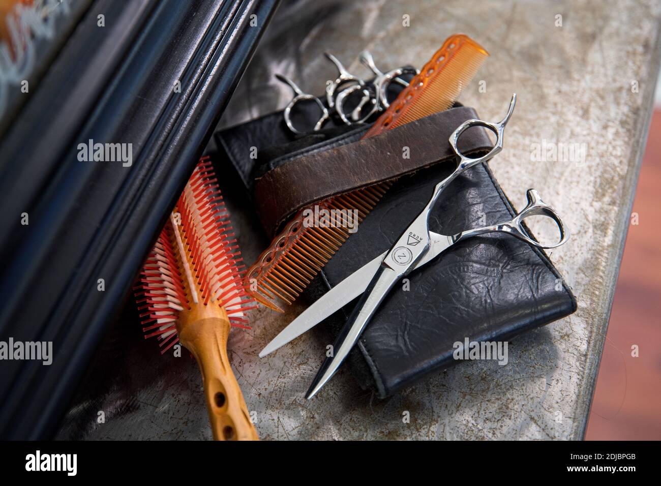 Hairdressing professional tools: comb, hairbrush, scissors and leather case displayed on a shelf in front of the mirror Stock Photo