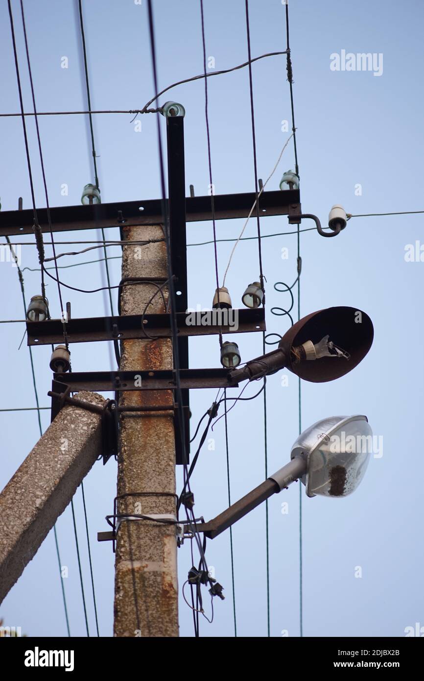 old stone pillar with wires and broken lamp on the blue sky background. Stock Photo