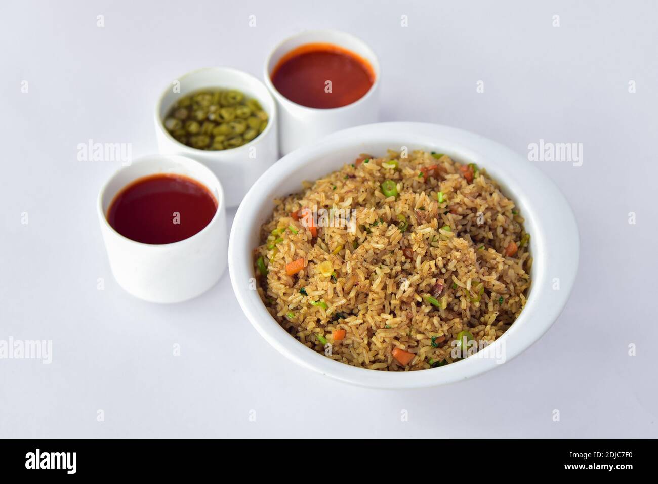 fried rice in a bowl with sauces in a white background. schezwan fried rice in white background with red sauces and peppers. Stock Photo