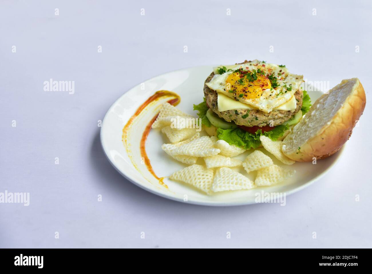 burger on a plate with chips. burger with patty and vegetables like cucumber, tomatoes, lettuce and half boiled egg and chips. Stock Photo