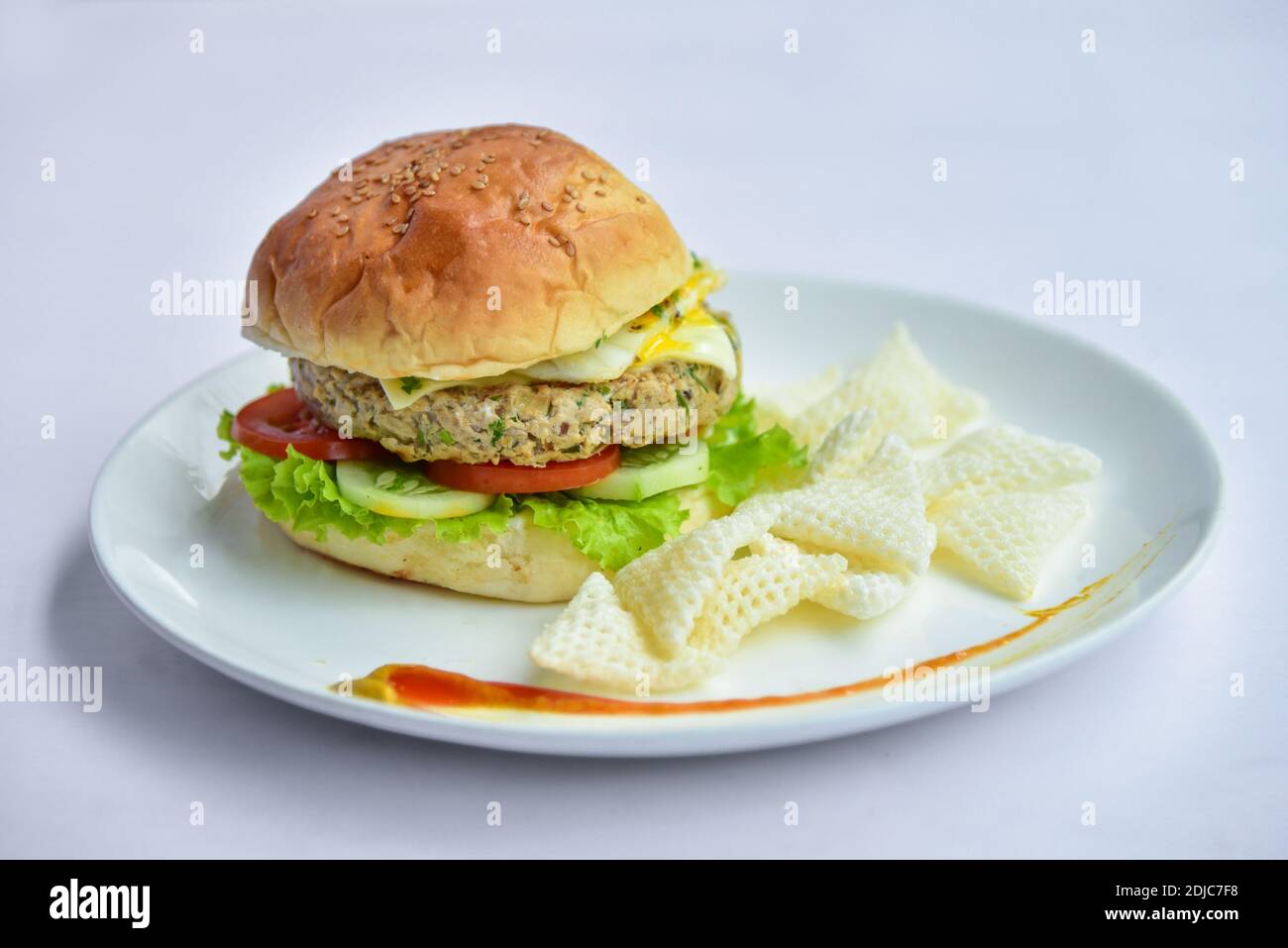 burger on a plate with chips. burger with patty and vegetables like cucumber, tomatoes, lettuce and half boiled egg and chips. Stock Photo