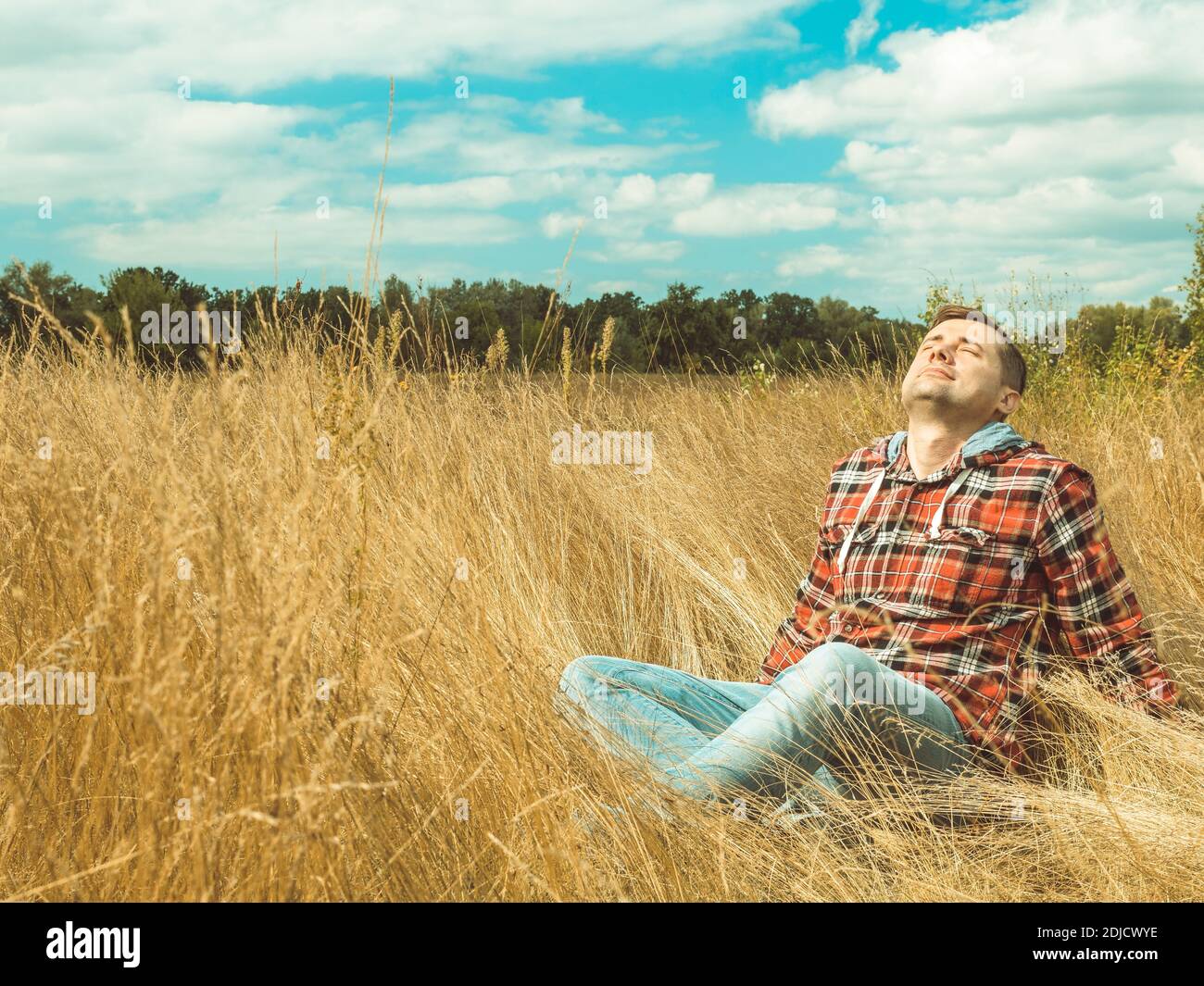Young man relaxes sitting in nature in grass in autumn. Stock Photo