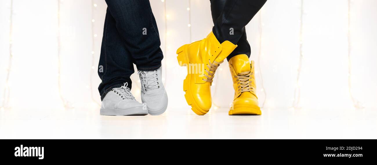 Banner made with unrecognizable people in bright yellow boots and sneakers standing against white wall with fairy lights Stock Photo