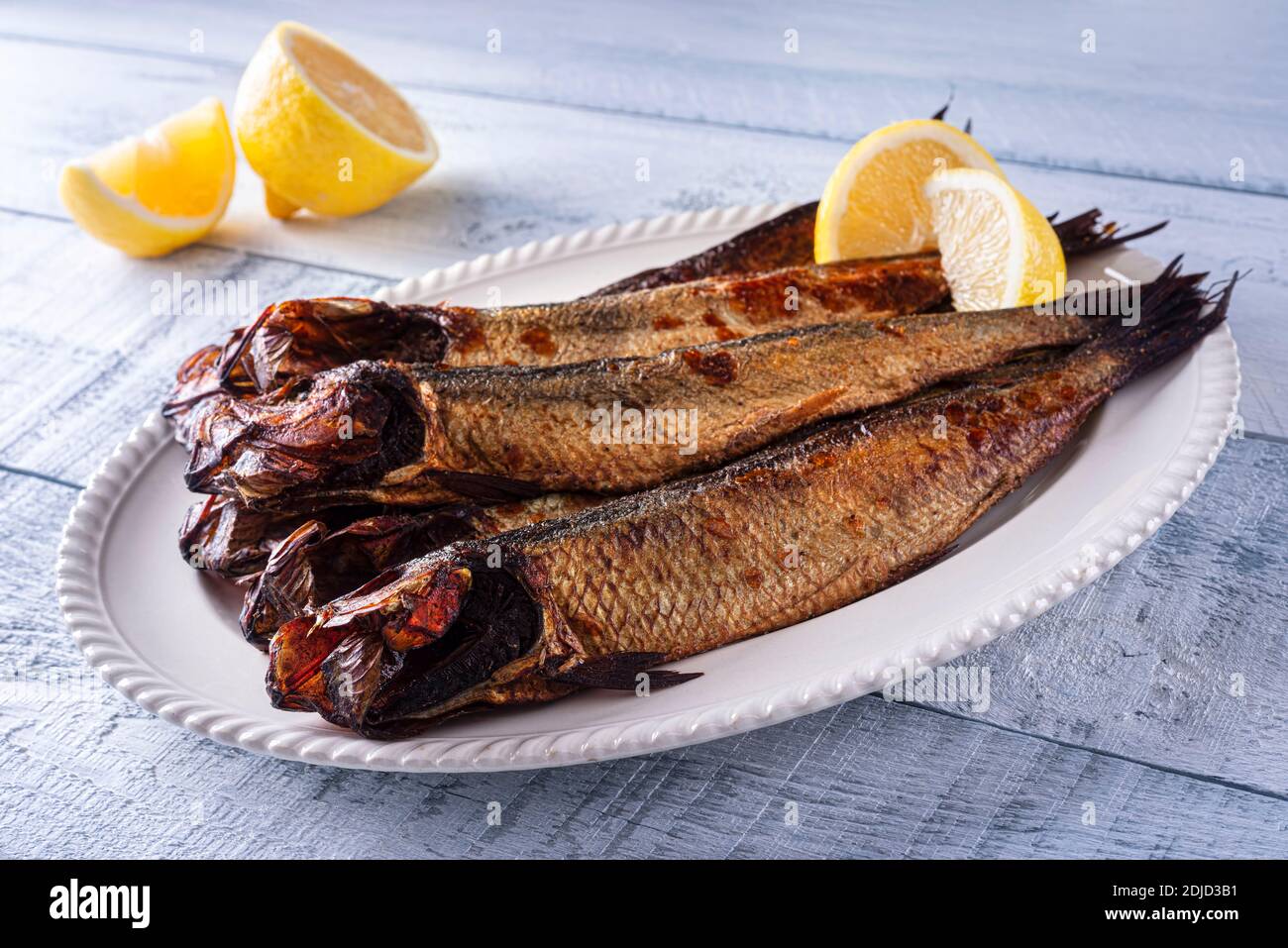 A plate of delicious smoked herring kippers with lemon on a wood table top. Stock Photo