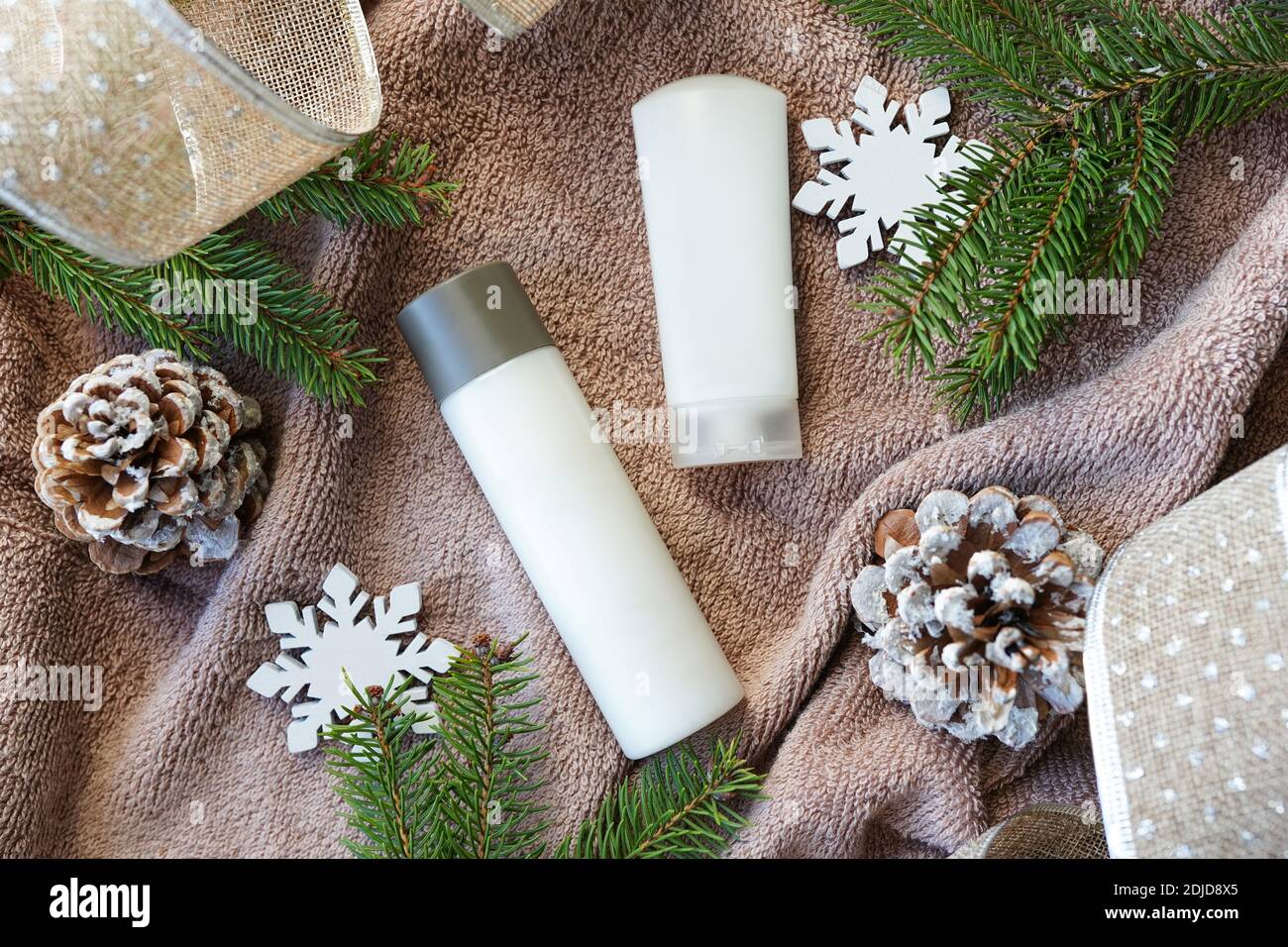 Winter skin care cosmetics. White bottle, jar or moisturizer cream, gel or shampoo with christmas tree and snowflakes on towel background. Flat lay, t Stock Photo