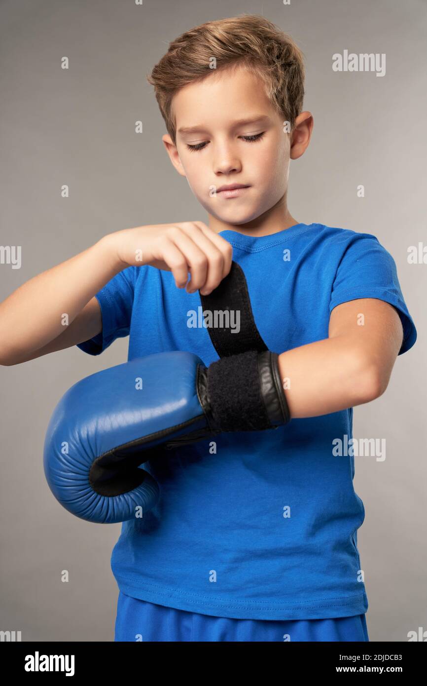 Serious cute boy preparing hands for boxing training while standing