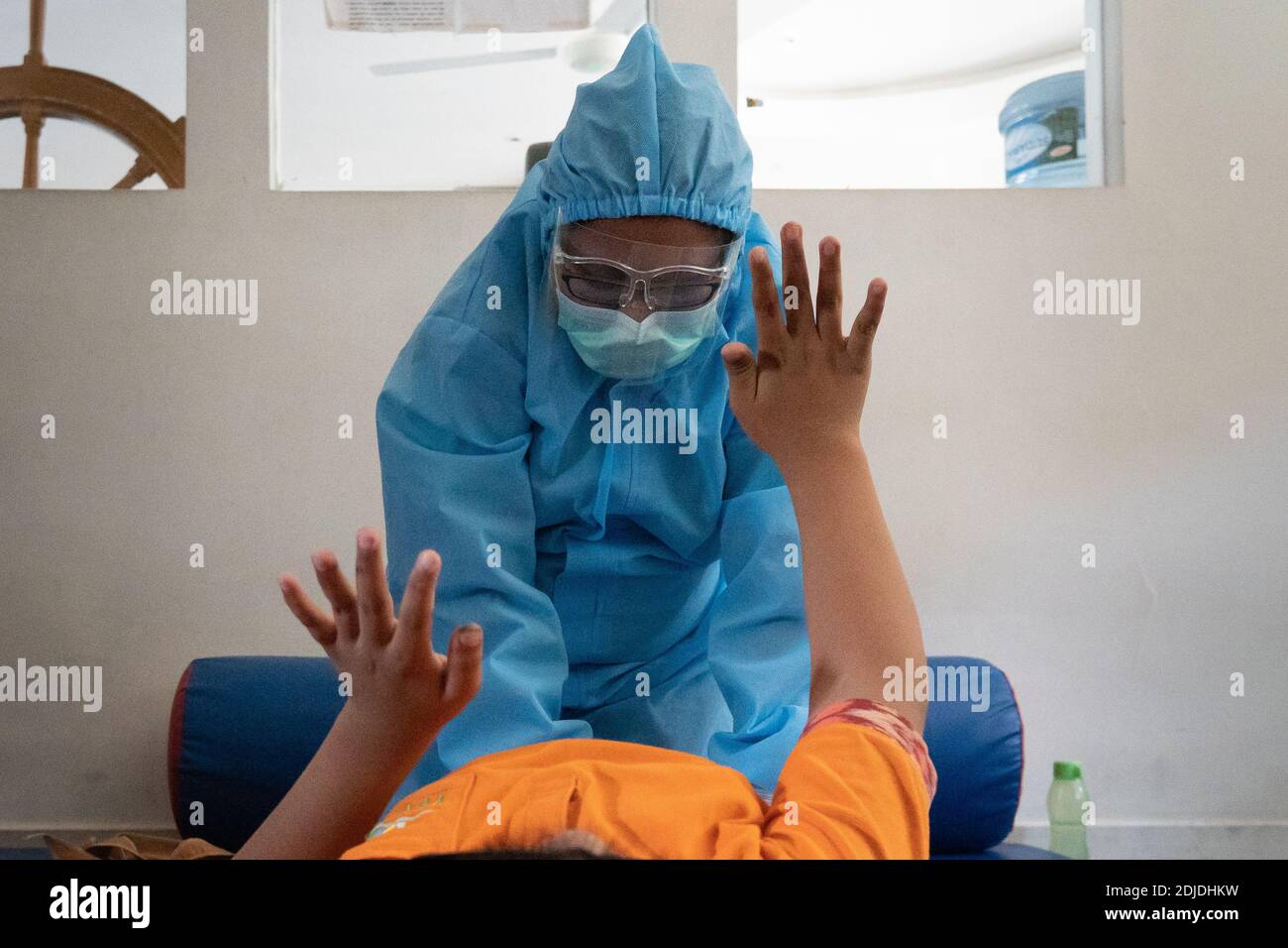 BALI/INDONESIA-OCT 23 2020: a child with a physical disability is doing physical therapy. They wear masks and hamzat suit to avoid the spread of the C Stock Photo