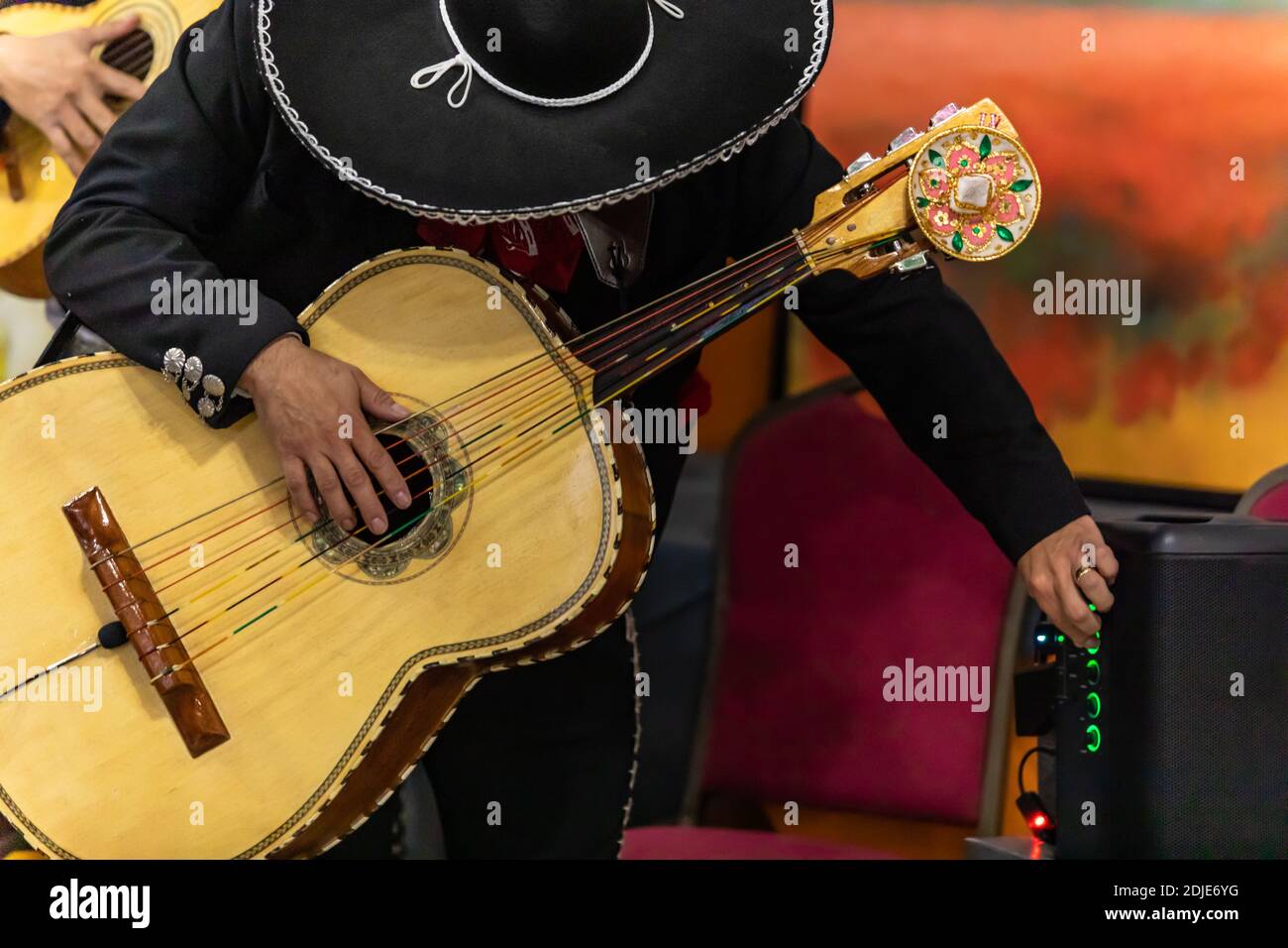 Selective focus of hands of young man mariachi, holding and playing acoustic bass guitar with orchestra and ajusting volume during the festival of dia de los muertos Stock Photo