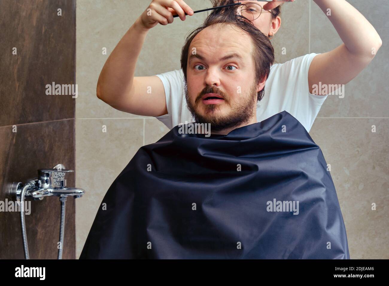 A woman gives a haircut to a man in the bathroom, closeup Stock Photo