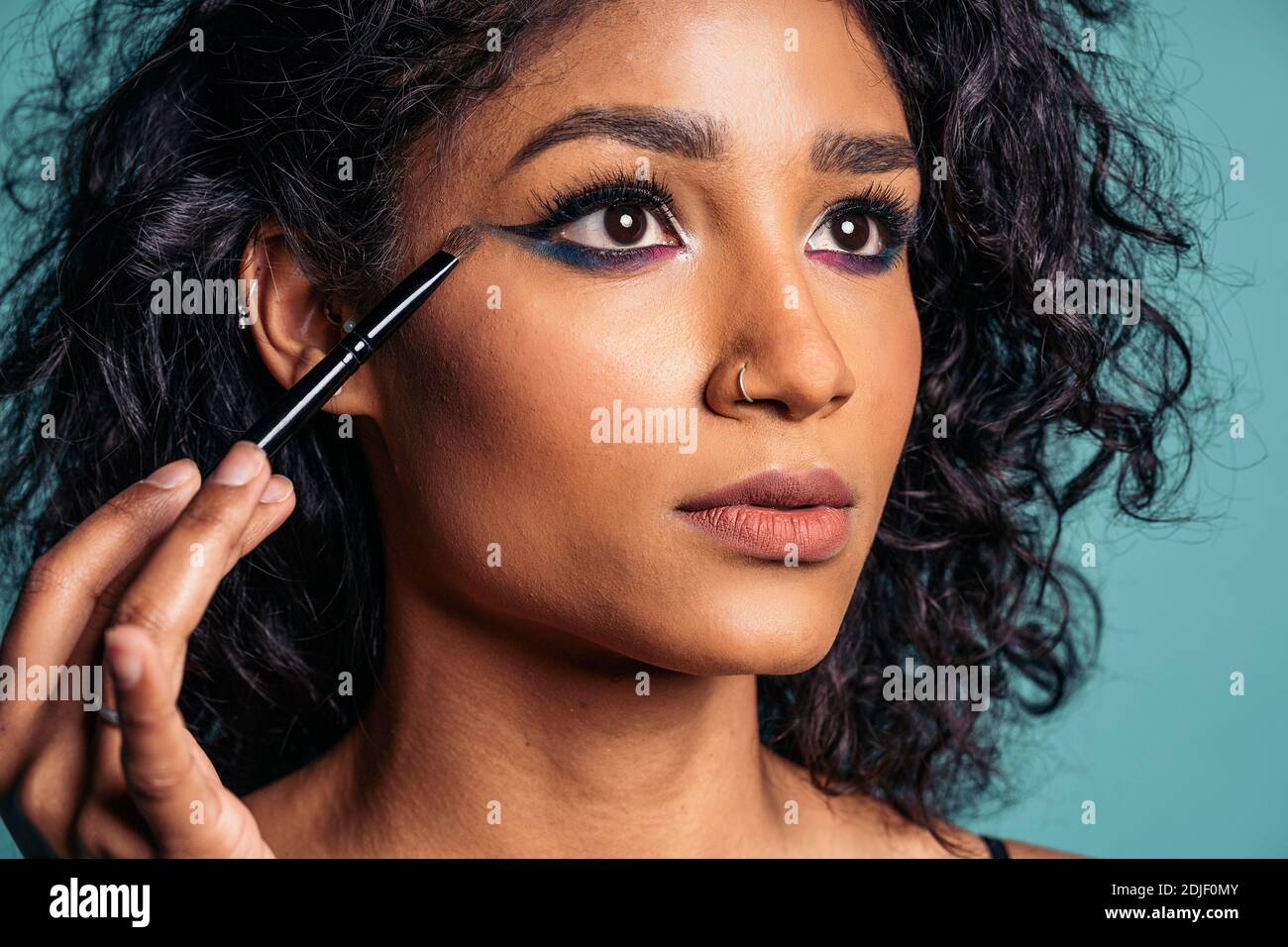 Stock photo of young hispanic woman wearing cool makeup using eye brush and looking to the side. Stock Photo