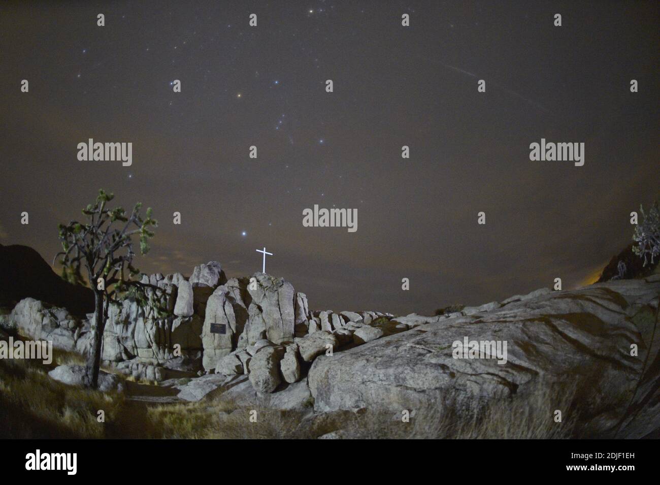 Mojave National Preserve, California U.S. 13th Dec, 2020. A Geminid meteor is seen visible through a thin layer of clouds as it streaks over the White Cross World War I Memorial on December 13, 2020. The meteor display, known as the Geminid meteor shower because it appears to radiate from the constellation Gemini, is thought to be the result of debris cast off from an asteroid-like object called 3200 Phaethon. The shower is visible every December. Credit: David Becker/ZUMA Wire/Alamy Live News Stock Photo