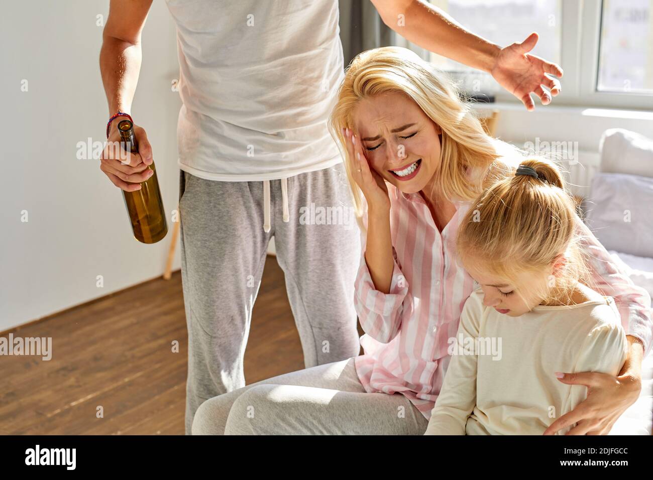 blond woman and child girl sits suffering from cruelty of father, abusive relationships concept, man is screaming and punishing members of family Stock Photo