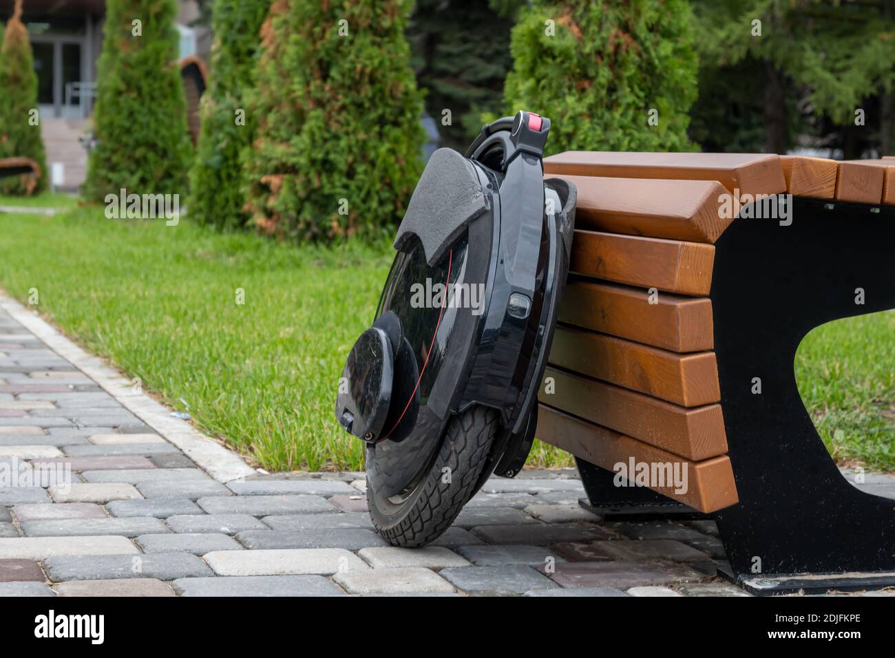 Black electric mono wheel, innovative personal vehicle, self-balancing electric unicycle, ecological urban transport of the future near a wooden bench Stock Photo