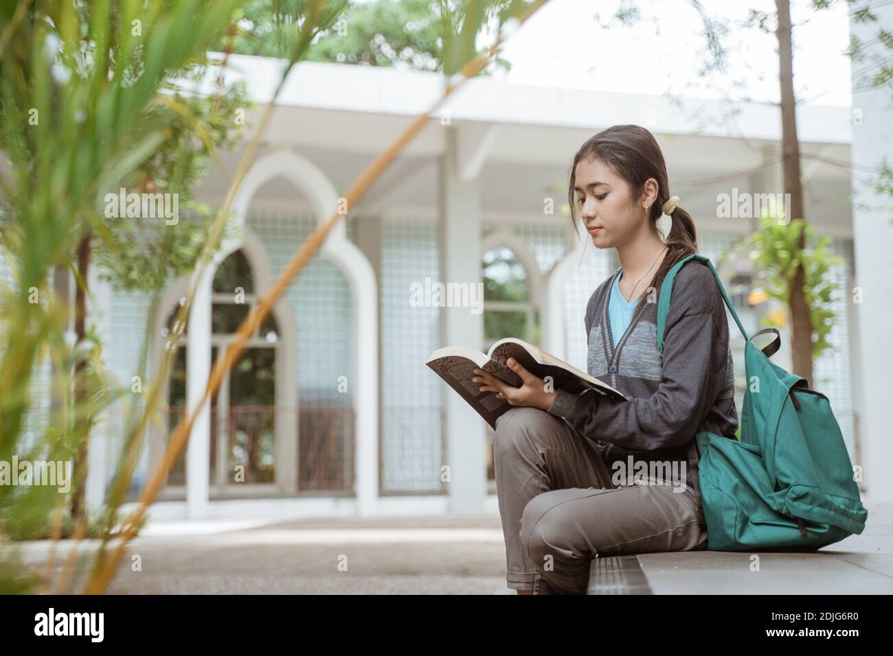 Portrait of happy female student reading holding book on the campus ...