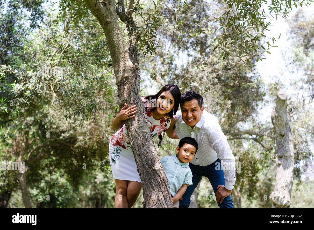 Happy family with man, woman and child leaning on tree in city park. Copy space Stock Photo